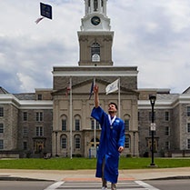 Man throws cap in front of Hayes Hall. 