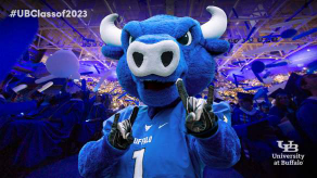A photo backdrop graphic that includes Victor E. Bull with horns up in front of a crowd of graduates wearing caps and gowns in Alumni Arena. 