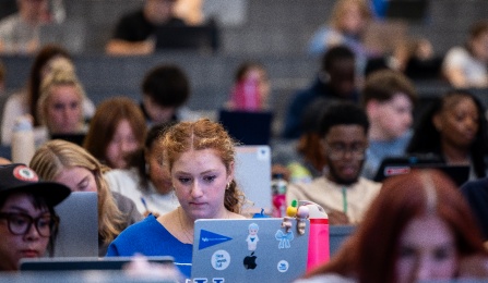 students in a large lecture hall using laptops. 