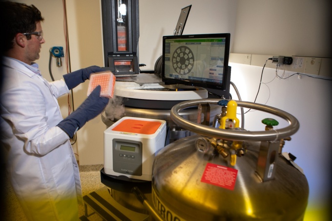 A researcher in a lab coat loads a biological sample into a piece of lab equipment. 