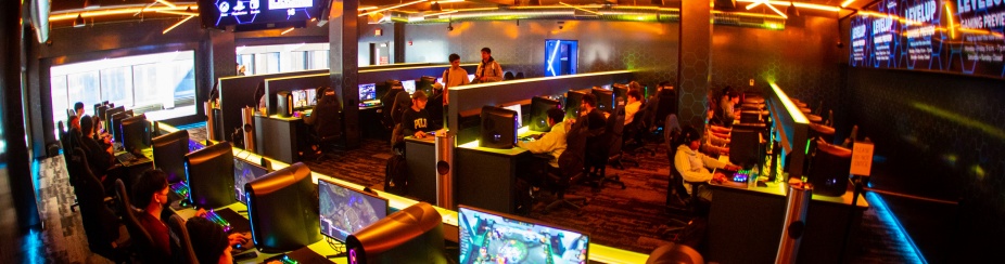 Banks of gaming machines host student gamers in a colorfully-lit space. 