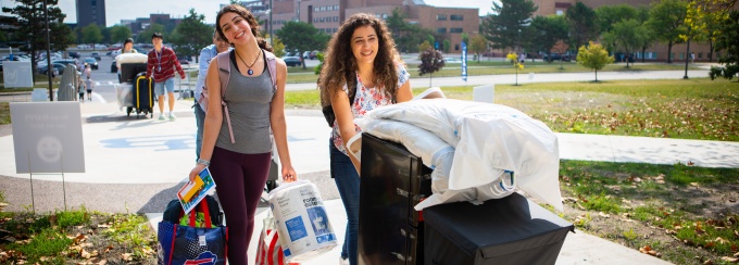 A student smiles as she moves into her residence hall. 