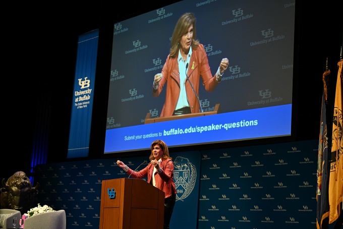 Hoda Kotb at the podium, her image on a large projection screen behind her. 