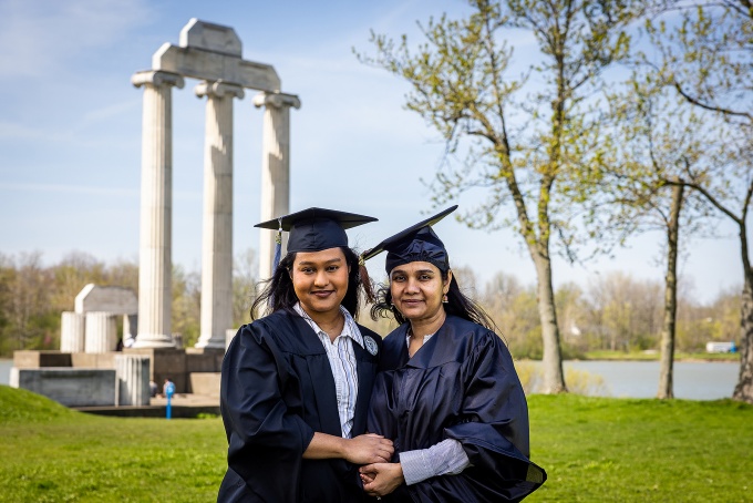 Maheea Sayeed and Farzana Moid dressed in caps and gowns, Baird Point in the background. 