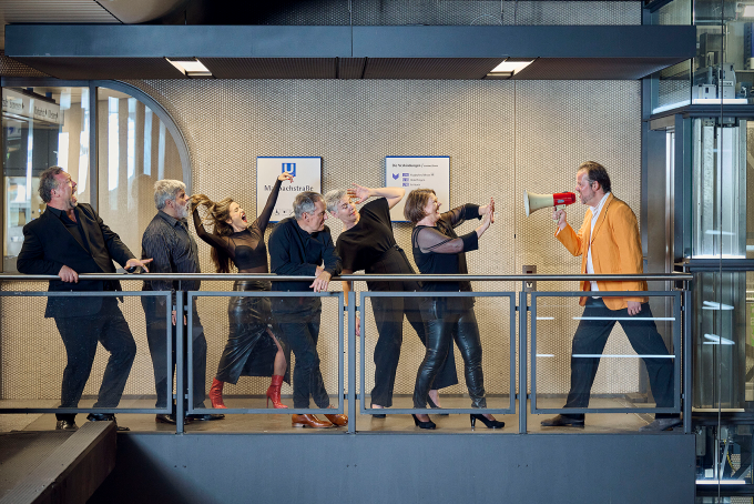 Neue Vocalsolisten Stuttgart pictured on a subway platform, one member holds a megaphone. 