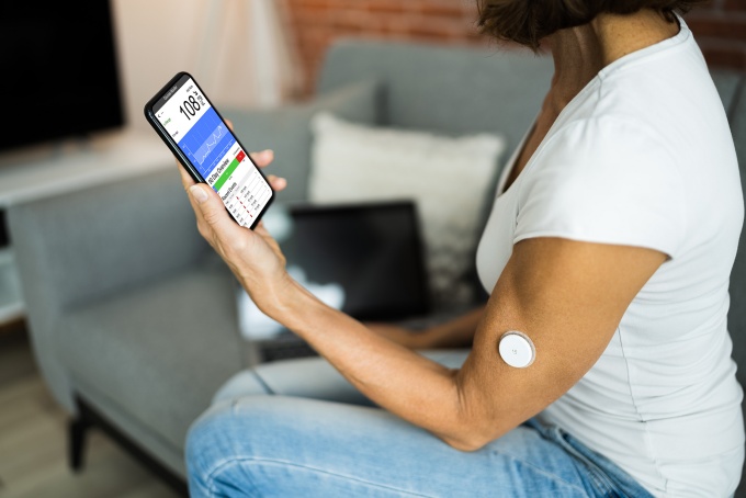 A woman holds a continuous glucose monitor. 