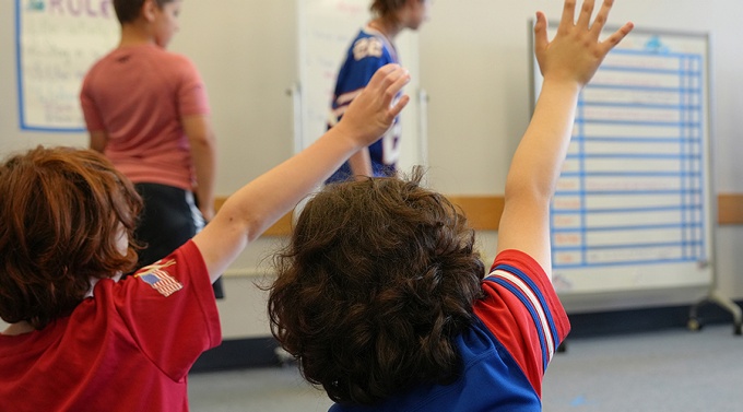 Children in a classroom raising their hands. 
