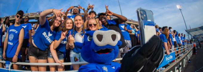 Victor E. Bull takes a selfie with several students wearing UB gear at a football game. 