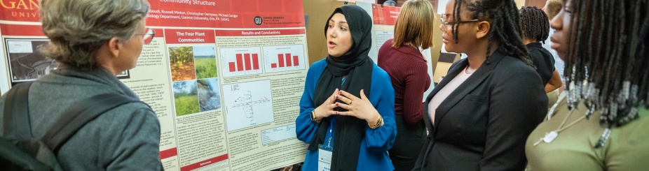 A presenter stands in front of her poster explaining her research to 3 attendees. 