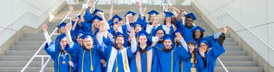 Students standing on stairs in caps and gowns. 