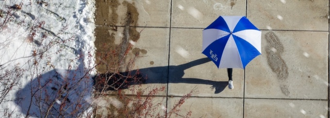 A person walks on a path on North Campus with a UB umbrella. Photo Illustration: Douglas Levere. 