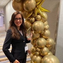Susan Davis O’Rourke, Assistant Director of Student Engagement stands next to gold ballon arch while holding an ACPA award. 