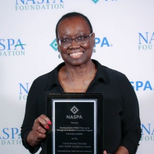 Dr Sharon Mitchel holding a black and silver NASPA award. 