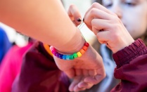 Zoom image: Student putting a rainbow bead bracelet on another student's arm.
