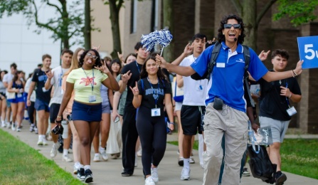 Student in a UB shirt leading a large group of students walking outside. 