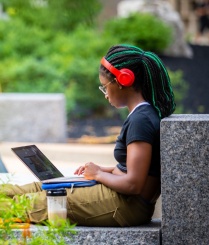 Person wearing headphones, sitting outside with a laptop. 