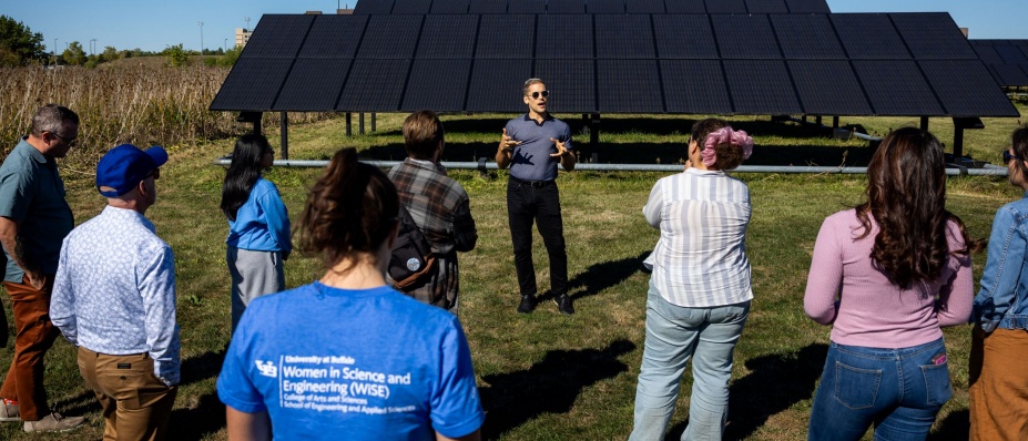 A man speaking to a group of people in front of solar panels.