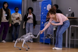A girl excitingly shaking the hand of a robot dog.