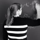 female student performs math problem on chalkboard. 