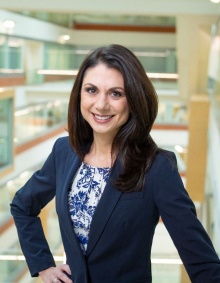 Professional portrait of Dr. Meka in a black blazer, standing in front of a railing that over looks the inside of the Jacobs School of Medicine and Biomedical Sciences. 