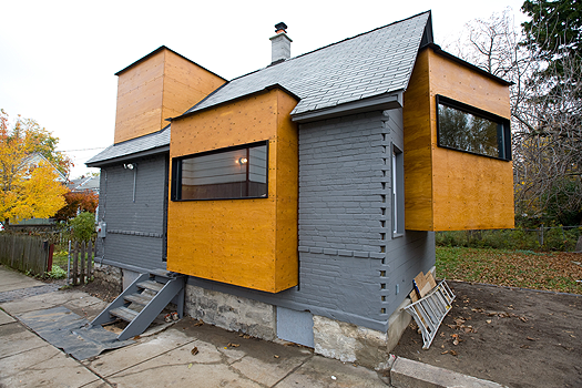 the side of a small brick house with cube-shaped, wooden rooms jutting out from it