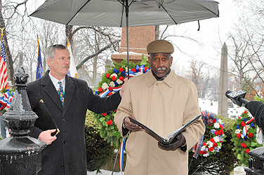 William Regan, director of the Office of Special Events, holds an umbrella to shield Willie Evans, Ed.B ’60, a special advisor to the UB Alumni Association Board of Directors, from the elements as Evans delivers the commemorative address at the annual gravesite celebration of the anniversary of the birth of Millard Fillmore. Photo: NANCY J. PARISI